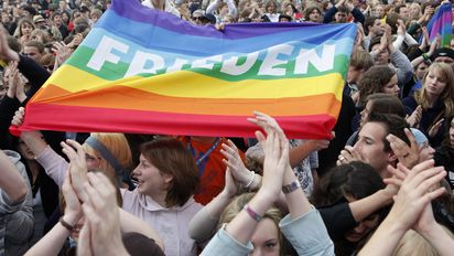 Menschenmenge beim Kirchentag, in der Mitte wird eine Regenbogenflagge mit dem Aufdruck frieden hochgehalten.