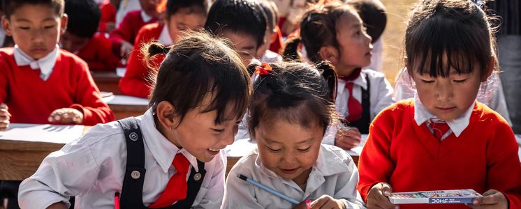 Asiatische Schulkinder schreiben mit Stiften auf Blättern.