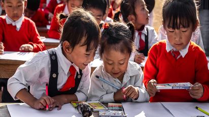 Asiatische Schulkinder schreiben mit Stiften auf Blättern.