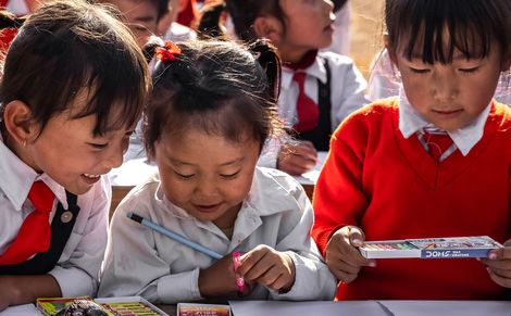 Asiatische Schulkinder schreiben mit Stiften auf Blättern.