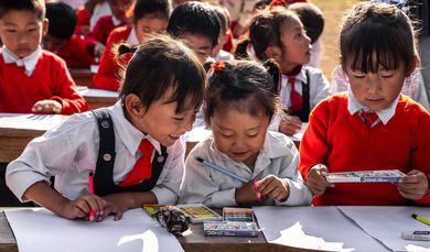 Asiatische Schulkinder schreiben mit Stiften auf Blättern.