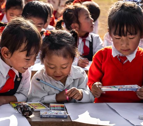 Asiatische Schulkinder schreiben mit Stiften auf Blättern.