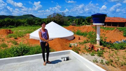 Frau steht auf einem gepflasterten Platz im Hintergrund eine Beton-Zisterne
