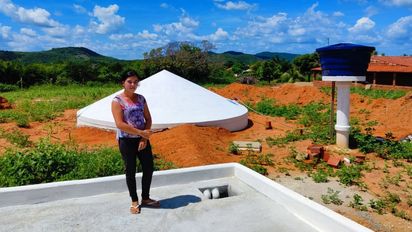 Frau steht auf einem gepflasterten Platz im Hintergrund eine Beton-Zisterne