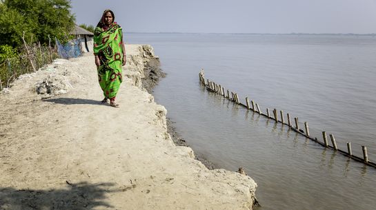 Eine Frau geht über einen Deich in Bangladesch.