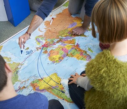 zwei Kinder sitzen vor einer Weltkarte auf die etwas eingezeichnet wird 