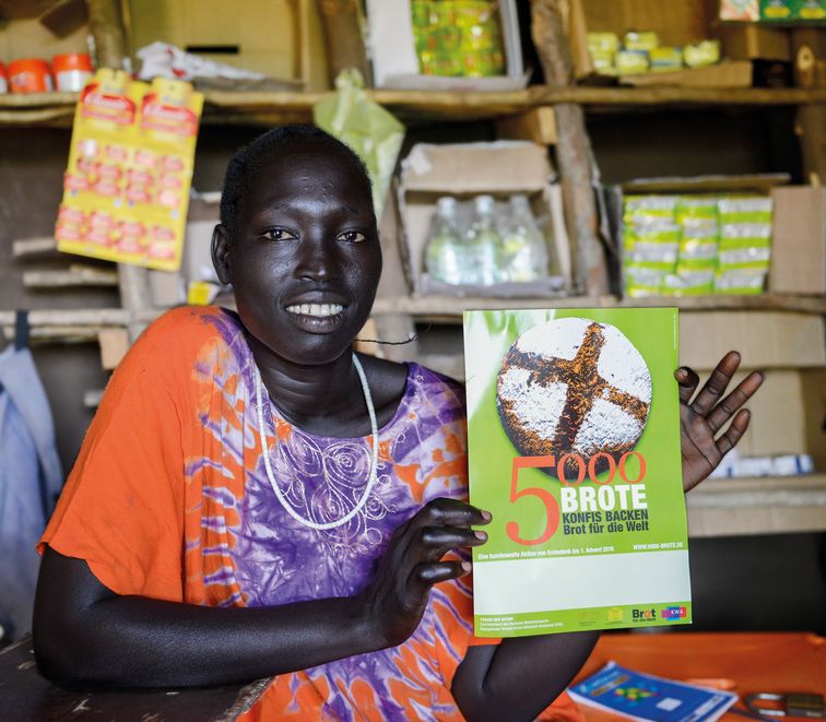  Ajulu Obang mit einem Plakat zur Aktion "5000 Brote" in der Hand