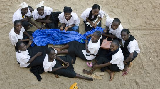 Elf Schneider-Schülerinnen sitzen im Sand mit einem blauen Seidentuch.