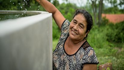 Eudacia Rivera steht lächelnd vor ihrem Wassertank