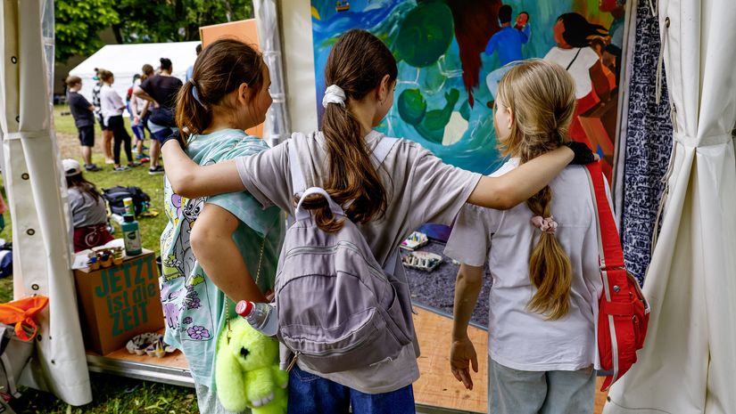 drei Kinder vor einem gemalten Bild am Stand der Brot für die Welt Jugend