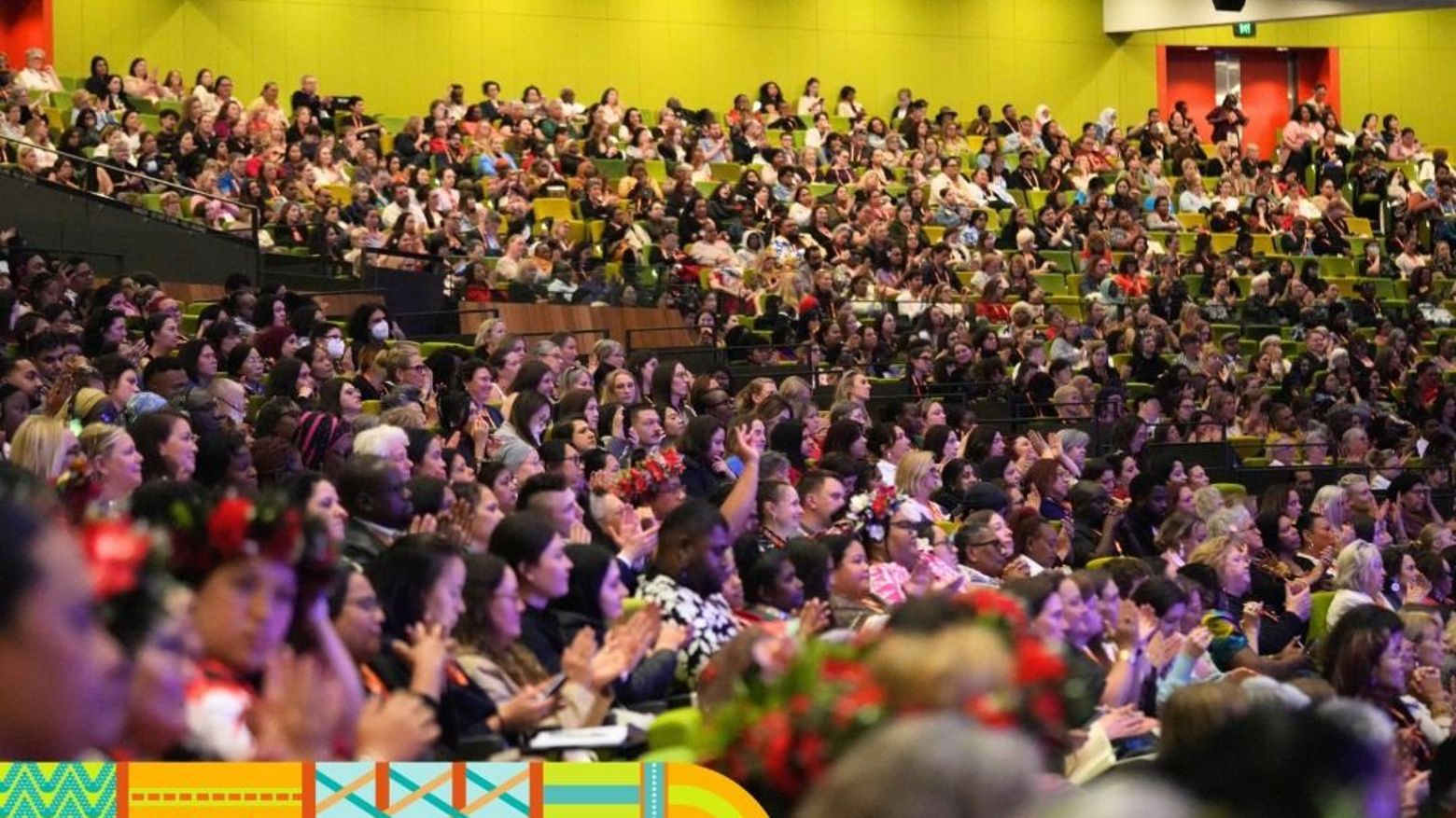 Menschen die im großen Plenum zusammen in einem Konferenzgebäude sitzen.