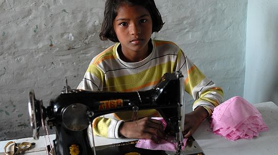 Ein Mädchen sitzt vor einer Nähmaschine. 