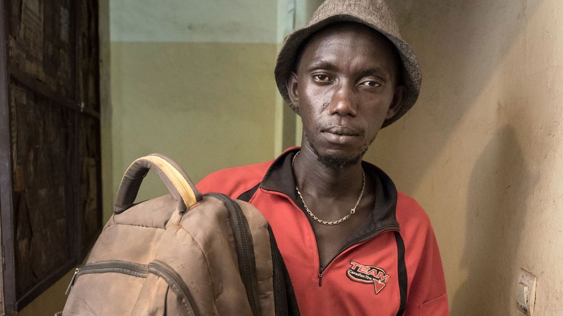 Portrait eines Mannes mit einem Rucksack in der Hand, trägt eine rote Jake und einen Hut 