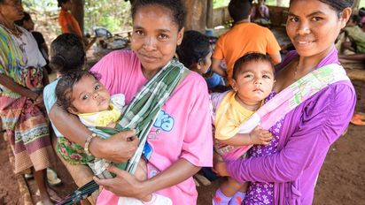 zwei Frauen mit Babys auf dem Arm, im Hintergrund mehr Kinder und Frauen