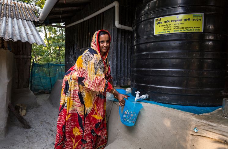 CCDB Bangladesch Khaleda Begum, profitiert von ihrer Regenwassergewinnung, die von CCDB gestellt wurde und kann jetzt sauberes Trinkwasser aus dem Wassertank zapfen. Die Menschen in den kleinen Siedlungen an den Fluessen in der Naehe von Shyamnagar in Sued Bangladesch, spuehren deutlich den Klimawandel. Der Meeresspiegel steigt und Daemme werden zerstört. Da durch werden Felder und die wichtigen Suesswasserteiche ueberflutet und versalzen. CCDB Bangladesch arbeitet an Suesswassergewinnungs-Projekten und sorgt dafuer, dass die Menschen nach und nach sauberes Trinkwasser erhalten.
