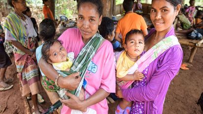 zwei Frauen mit Babys auf dem Arm, im Hintergrund mehr Kinder und Frauen