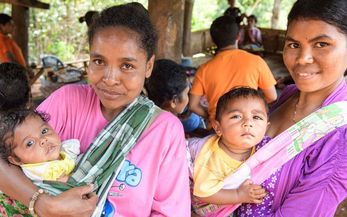 zwei Frauen mit Babys auf dem Arm, im Hintergrund mehr Kinder und Frauen