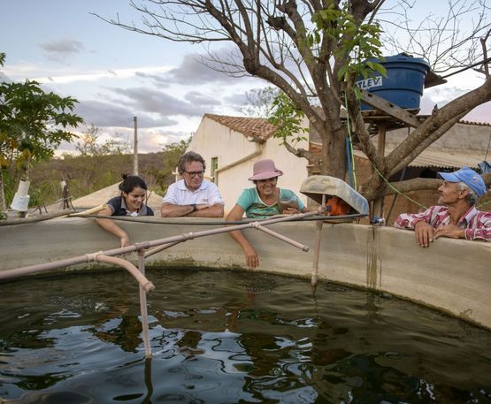 Die Kleinbauern Joselita Ramos Braz Souza (45, M) und Ehemann Luiz Braz Souza (51) fuettern die Fische in einer Wasserzisterne in der Gemeinde Jatoba nahe Carnaiba (Brasilien), am 13.12.18, waehrend Wasser- und Agrarexperte der DIACONIA, Afonso Fernandes Cavalcanti (53, 2.v.l.) zu schaut.DIACONIA, Partnerorganisation von Brot fuer die Welt, unterstuetzt Kleinbauern in der halbwueste Sertao mit Zisternen, Biogasanlagen, Know How in der Landwirtschaft und Bewaesserungssystemen.